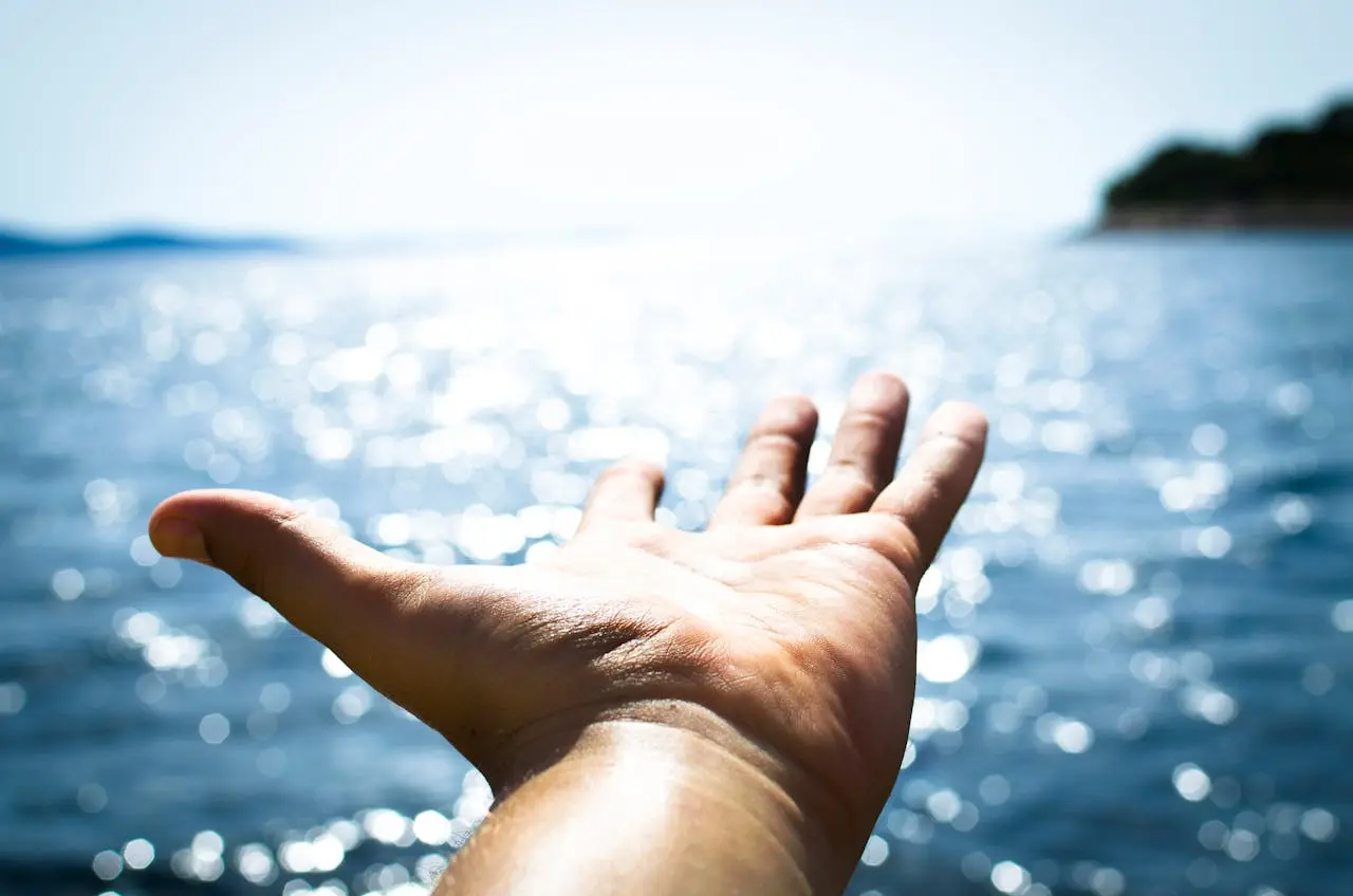 com o mar como fundo, uma mão está aberta como a pedir que a agarrem, ou a simbolizar a liberdade de algo